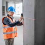 کارگر ساختمانی در حال اندازه گیری تیر حمایت با لیزر