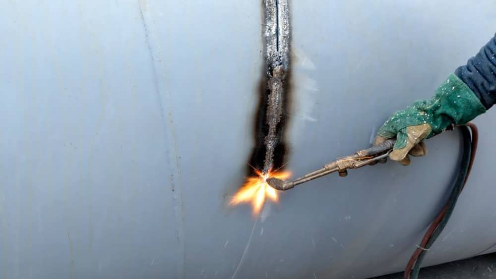 کارگر در حال برش روی صفحه فلزی با سوخت اکسیژن فرآیند برش شعله دستی است